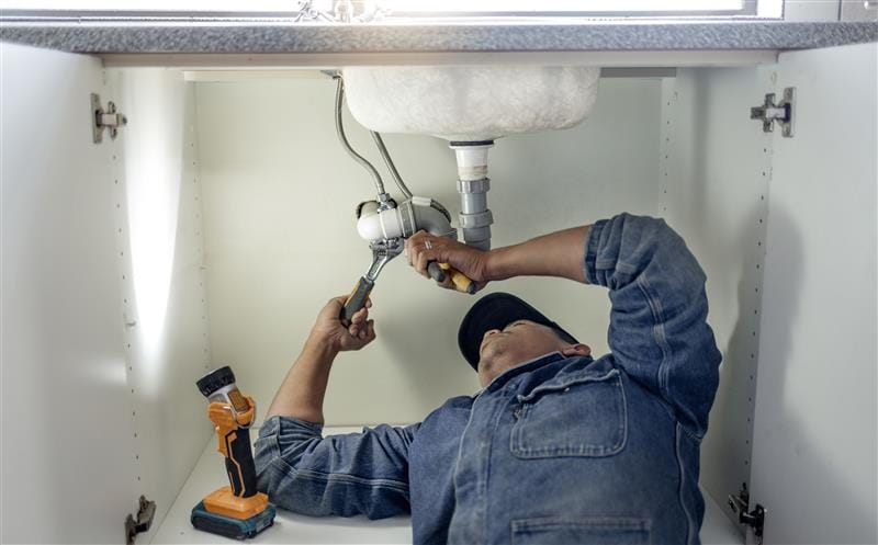Plumber repairing pipes beneath a bathroom sink in Wildwood
