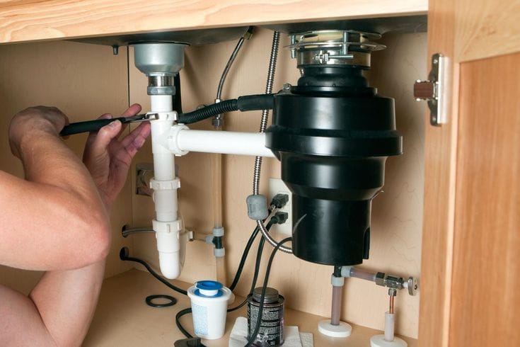 Plumber installing a garbage disposal beneath a kitchen sink in Wildwood