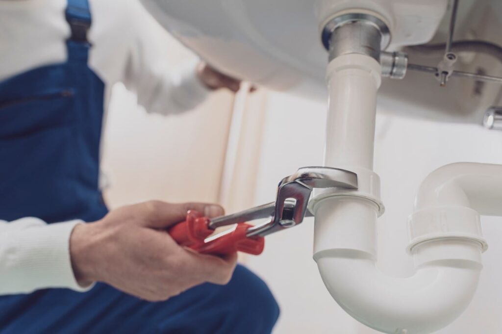 Plumber repairing a white drain pipe beneath a sink in Wildwood
