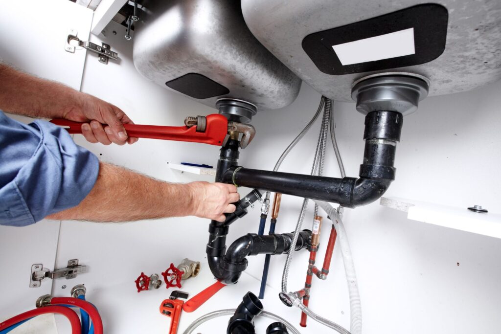 Plumber repairing drain pipes beneath a kitchen sink in Wildwood
